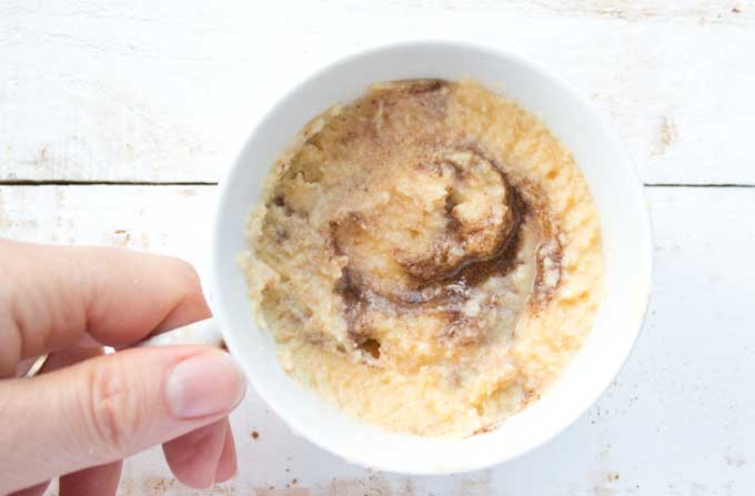 hand holding a mug with batter for a coconut flour mug cake with cinnamon swirl