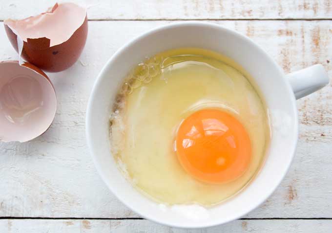 Wet ingredients for a coconut flour mug cake in a mug with egg shells on the side