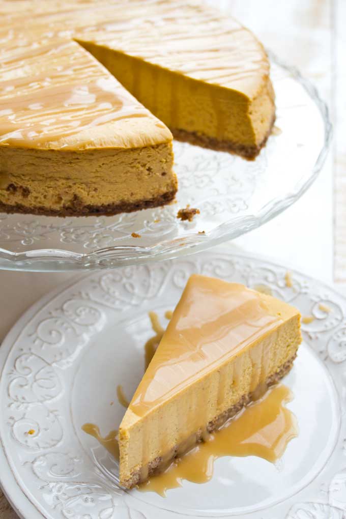 A pumpkin cheesecake on a cake stand and a slice of cake on a plate.