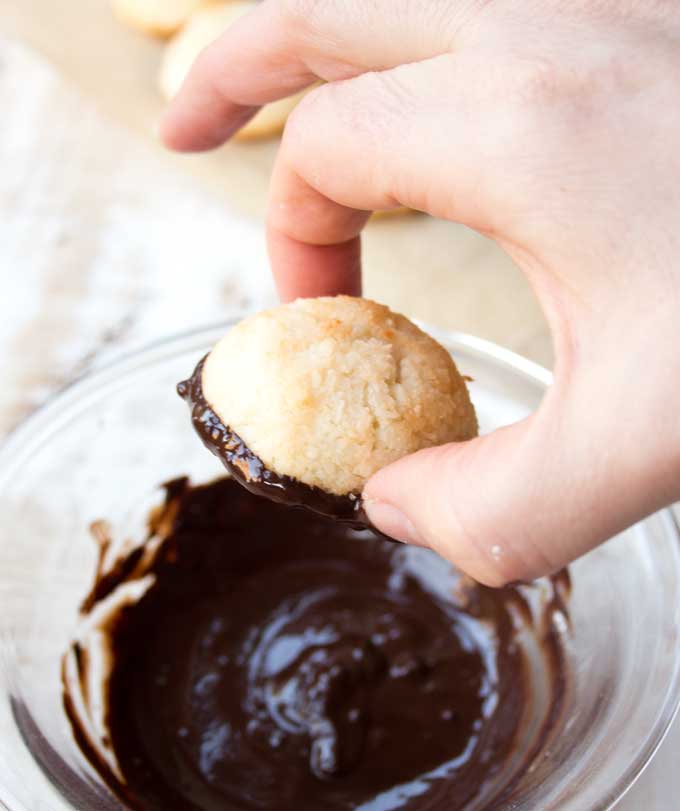 hand dipping a keto macaroon into melted chocolate
