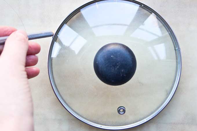 Hand tracing with a pencil around a saucepan lid, making a circle on parchment paper for Keto taco shells