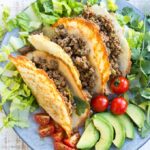 Three Keto taco shells on a plate filled with Taco ground beef and surrounded by salad on a plate