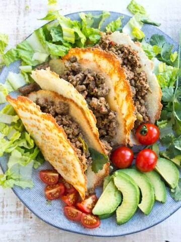 Three Keto taco shells on a plate filled with Taco ground beef and surrounded by salad on a plate