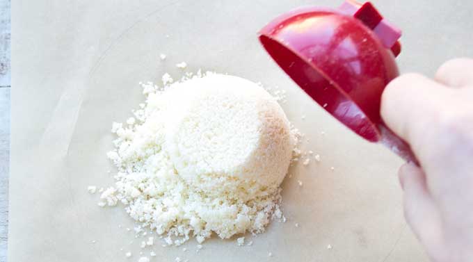 scooping a ¼ cup of keto taco shell mix onto the prepared parchment paper