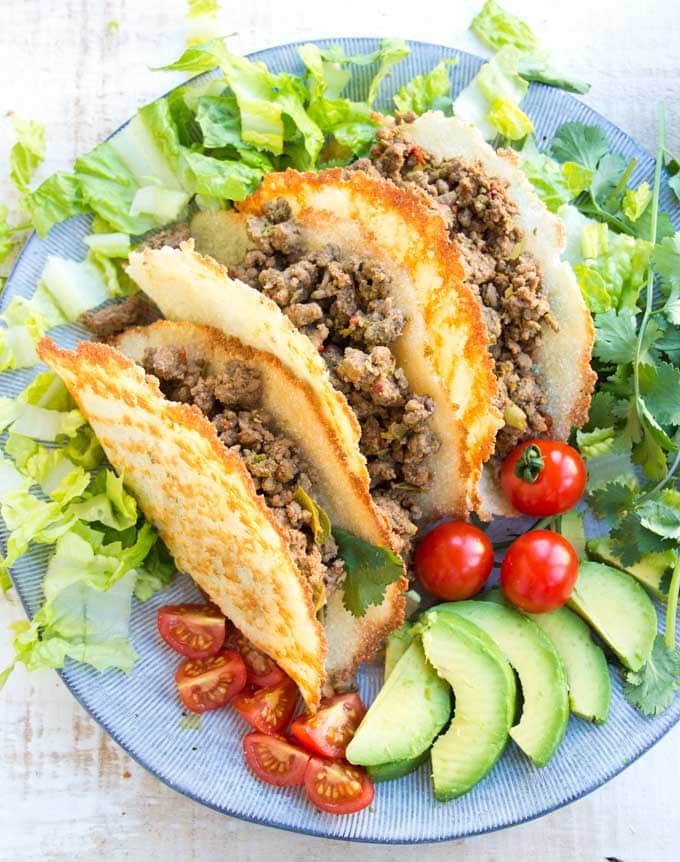 Three Keto taco shells on a plate filled with Taco ground beef and surrounded by salad on a plate