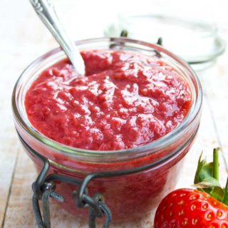 a jar or sugar free strawberry jam with a spoon inside and a strawberry in the foreground