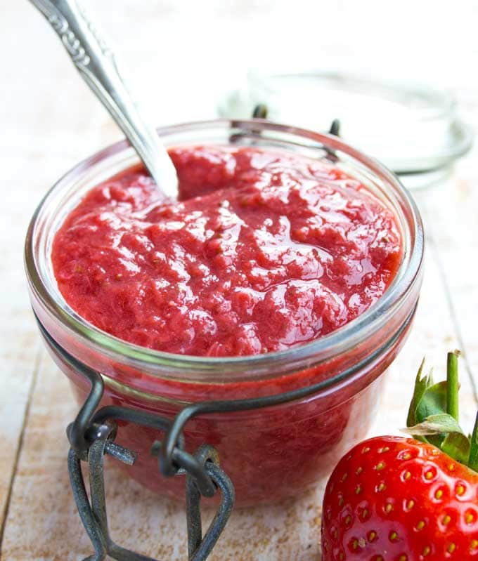 a jar or sugar free strawberry jam with a spoon inside and a strawberry in the foreground