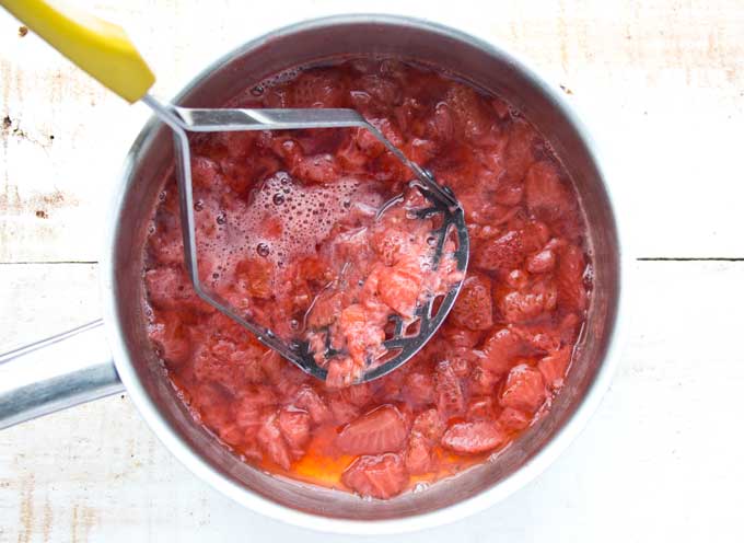 mashing softened strawberries with a potato masher in a saucepan