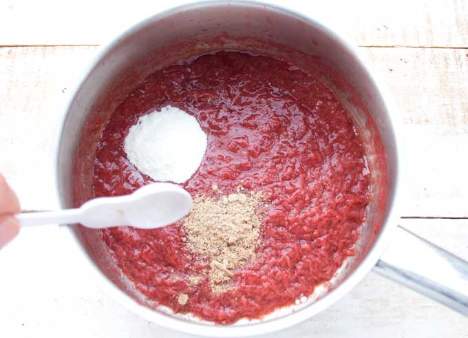 adding chia seeds and sweetener to a saucepan with sugar free strawberry jam with a spoon