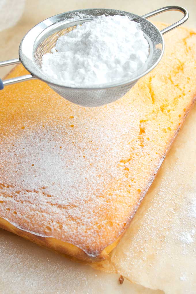 sprinkling powdered erythritol over the freshly baked Keto lemon cake