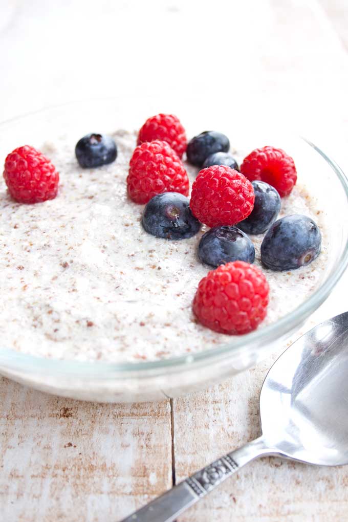 a bowl of keto low carb porridge decorated with blueberries and raspberries and a spoon