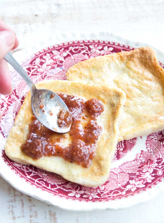 spreading sugar free strawberry jam onto toasted keto microwave bread with a spoon