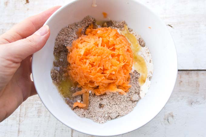 mixed dry ingredients for keto carrot cake plus melted butter and cream and a portion of grated carrots in a bowl before mixing