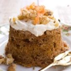a keto carrot cake turned out onto a plate decorated with cream cheese frosting, carrot shavings and crushed walnuts and a spoon