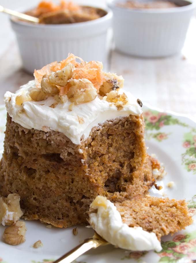 A carrot cake topped with cream cheese frosting on a plate with a spoon taking off a piece.