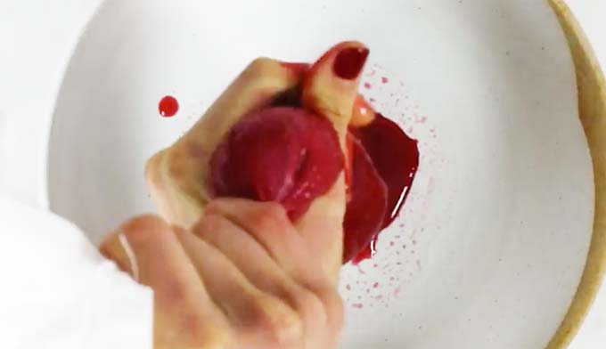 hands squeezing berry juice with a muslin into a bowl