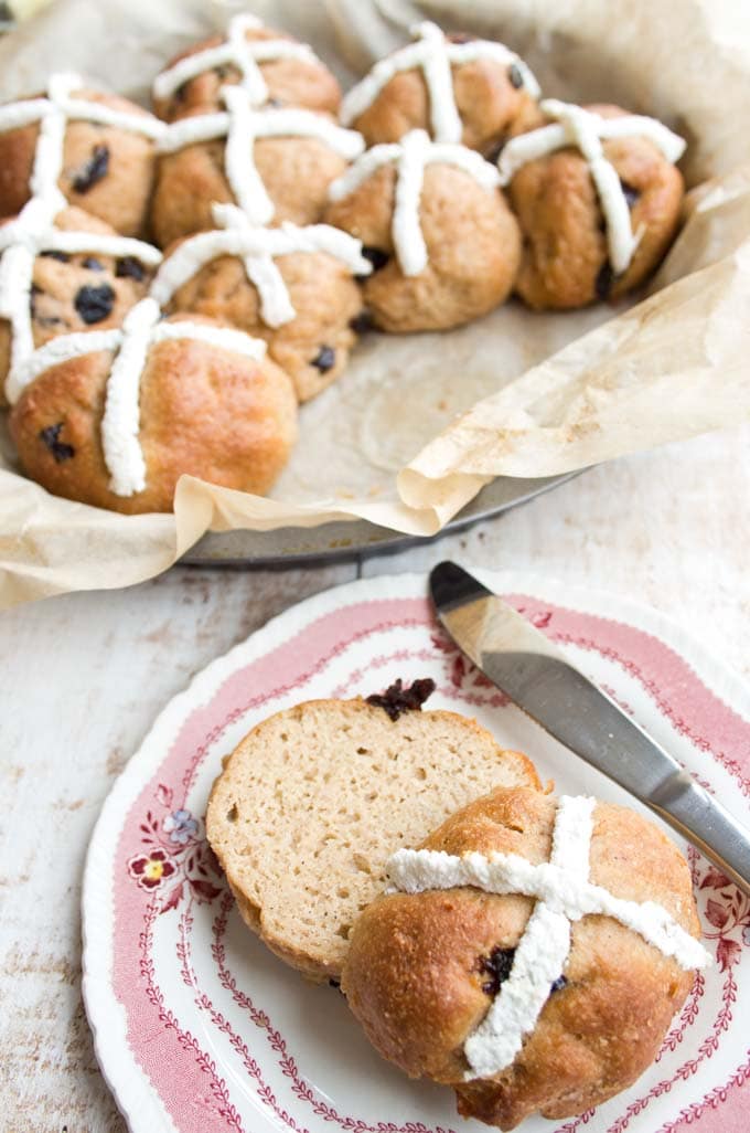 a plate with a hot cross bun cut in half with more hot cross buns in the background 