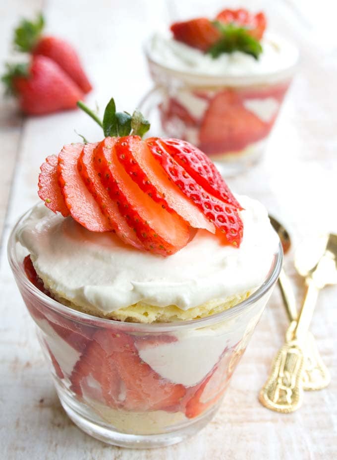 a glass cup filled with strawberry shortcake trifle and two golden spoons