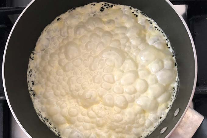 bubbling cream being reduced in a frying pan