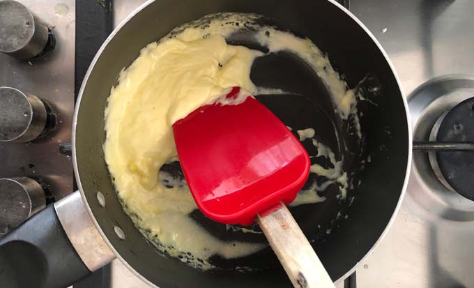 heavy cream, liquid reduced and firm, being scraped with a red silicone spatula in a frying pan