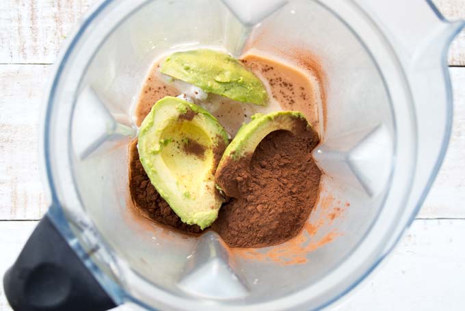 a blender with avocado halves, coconut cream and cocoa