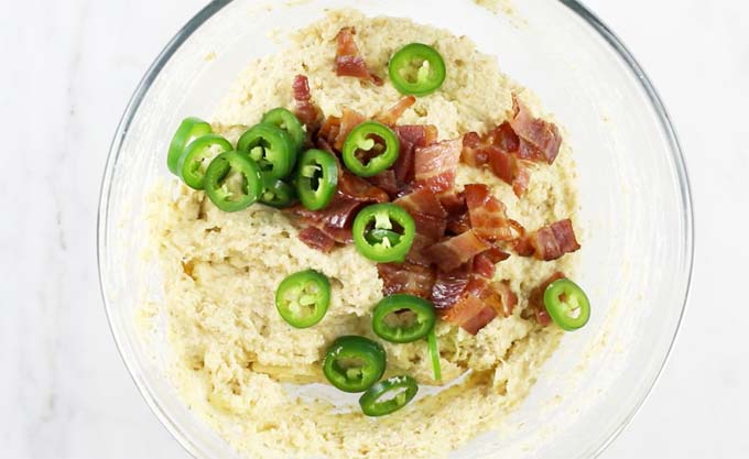 Jalapenos and grilled bacon pieces on top of the mixed batter in a glass bowl