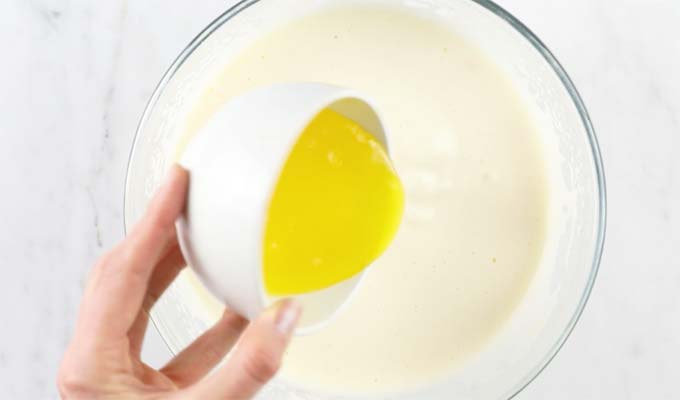 hand poring melted butter into a mixing bowl with whisked eggs