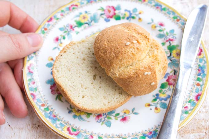 a dinner roll cut open on a small plate with a knife and a hand touching the plate