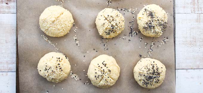 unbaked dinner rolls on a baking tray lined with parchment paper decorated with poppy seeds, sesame seeds and nigella seeds