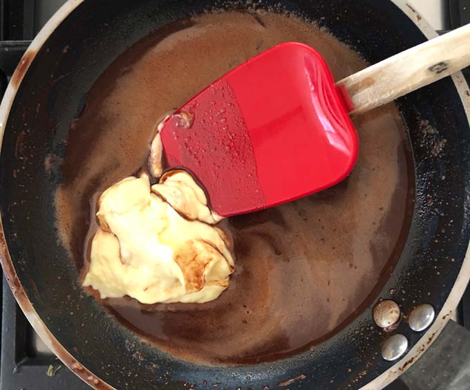 a red silicone spatula stirring double cream into liquid cocoa mass in a black pan