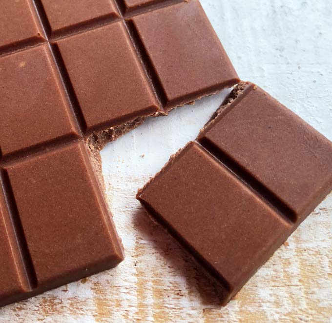 closeup of two pieces of keto milk chocolate tha have been broken off from a bar of homemade sugar free chocolate