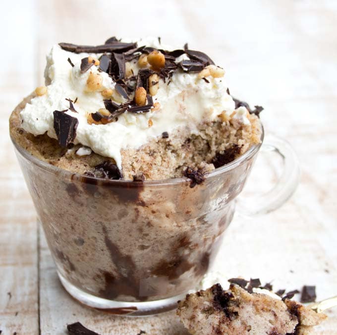 a peanut butter mug cake in a glass mug decorated with whipped cream with a spoonful taken out. 