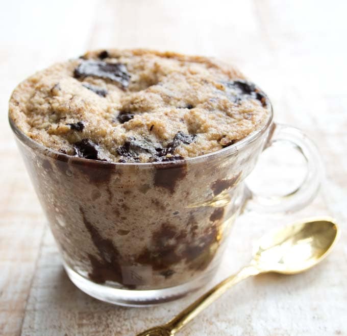 a peanut butter mug cake with chocolate chips in a glass mug and a golden spoon on the side