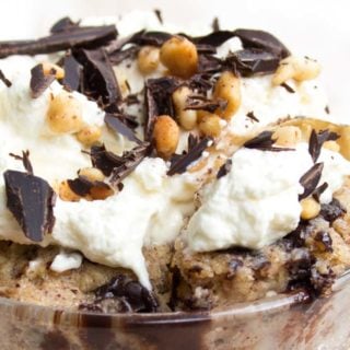 a peanut butter mug cake topped with whipped cream, peanut butter pieces and chocolate shavings and a spoon