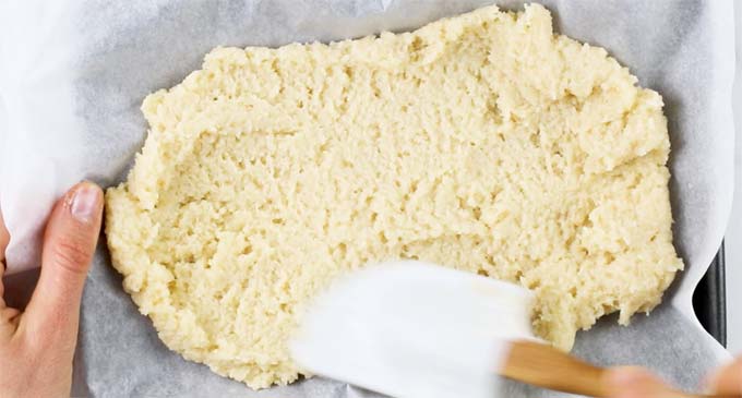 spreading batter for a tiramisu base onto a baking sheet lined with baking paper with a spatula