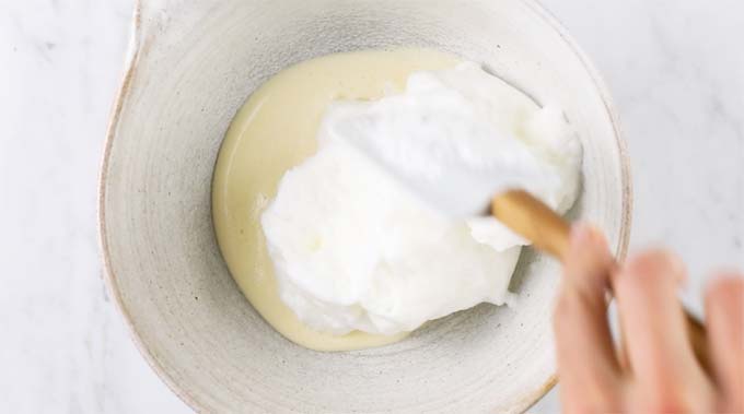 hand with a spatula mixing beaten stiff egg whites into frothed egg yolks in a mixing bowl