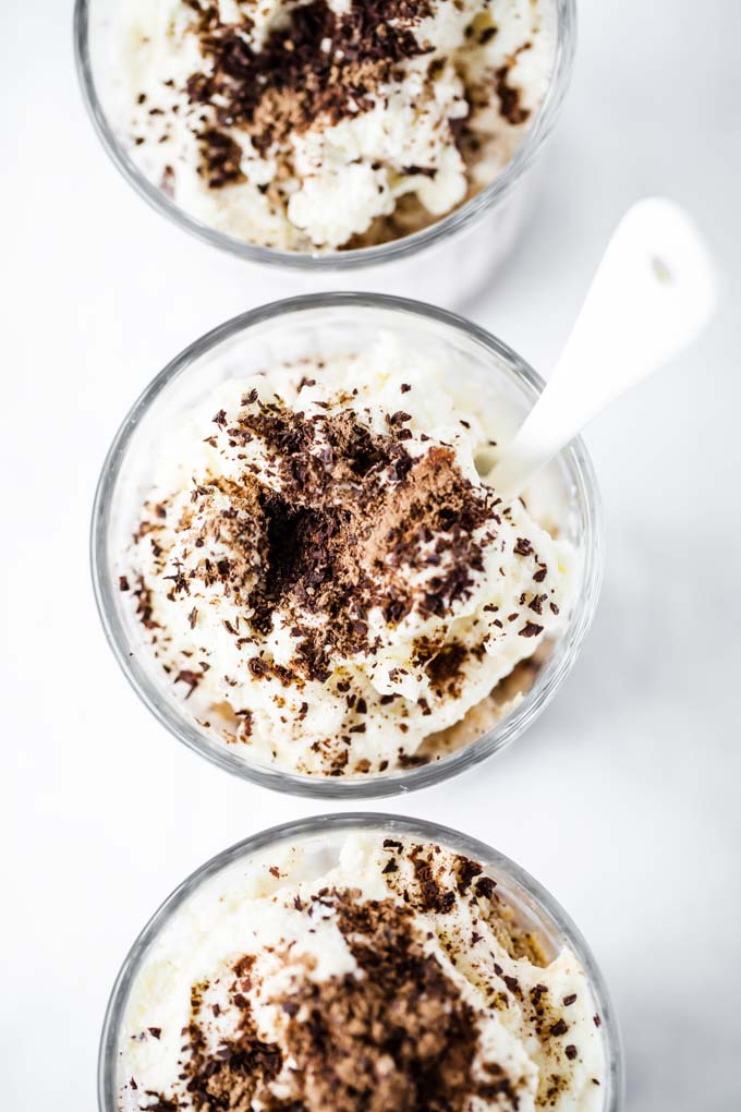 overhead shot of three glasses of tiramisu with a white spoon sticking out the middle glass
