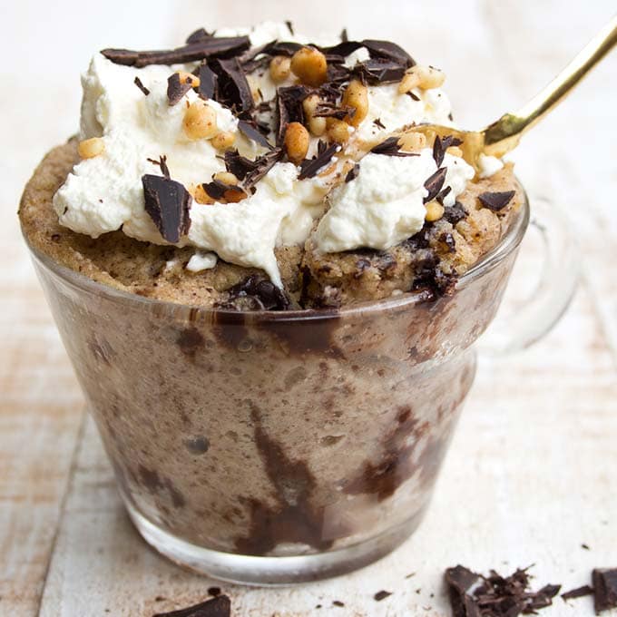 a peanut butter mug cake in a glass cup with whipped cream