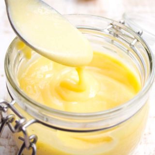 Keto lemon curd in a glass jar and a spoon with lemon curd dripping from it