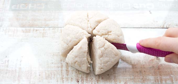 hand with knife cutting a dough ball into sic slices