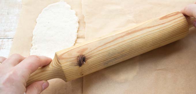 a wooden rolling pin flattening flatbreads through parchment paper