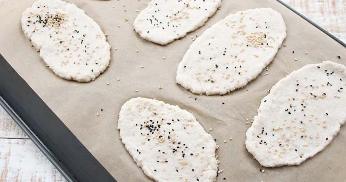 unbaked naan breads spinkled with nigella and sesame seeds on a baking tray lined with parchment paper