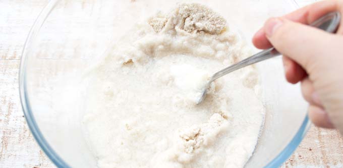 hand mixing dough with a fork in a glass bowl