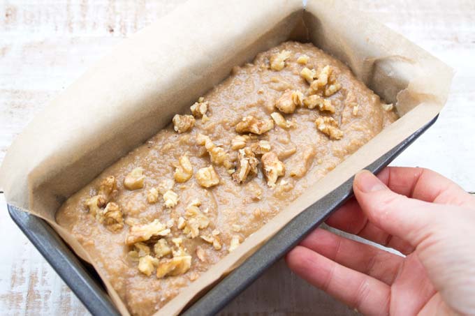 unbaked low carb banana bread in a bread tin lined with parchment paper and a hand
