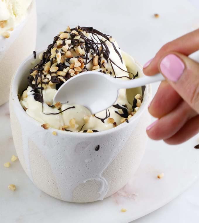 A hand taking a spoonful of vanilla ice cream decorated with chocolate and nuts