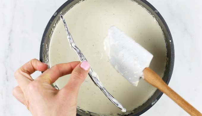 removing the vanilla bean from the cream mix after infusing in a pot by hand with a spatula