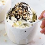 Vanilla ice cream topped with chocolate and nuts in a white ceramic pot and a spoon