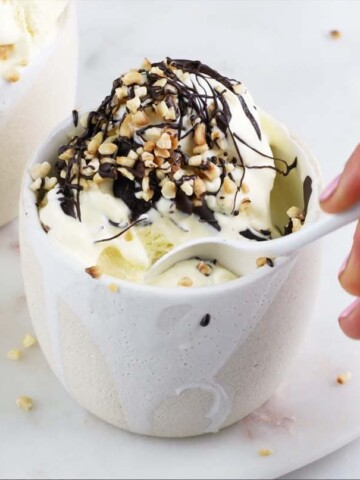 Vanilla ice cream topped with chocolate and nuts in a white ceramic pot and a spoon