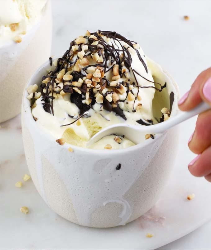 Vanilla ice cream topped with chocolate and nuts in a white ceramic pot and a spoon 