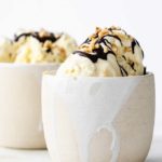 Two white ceramic dessert bowl with homemade low carb vanilla ice cream, decorated with a chocolate drizzle and chopped nuts